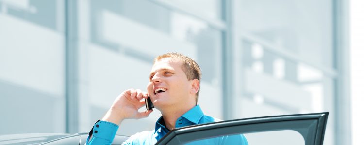 Businessman by the car car, talking on mobile phone, smiling