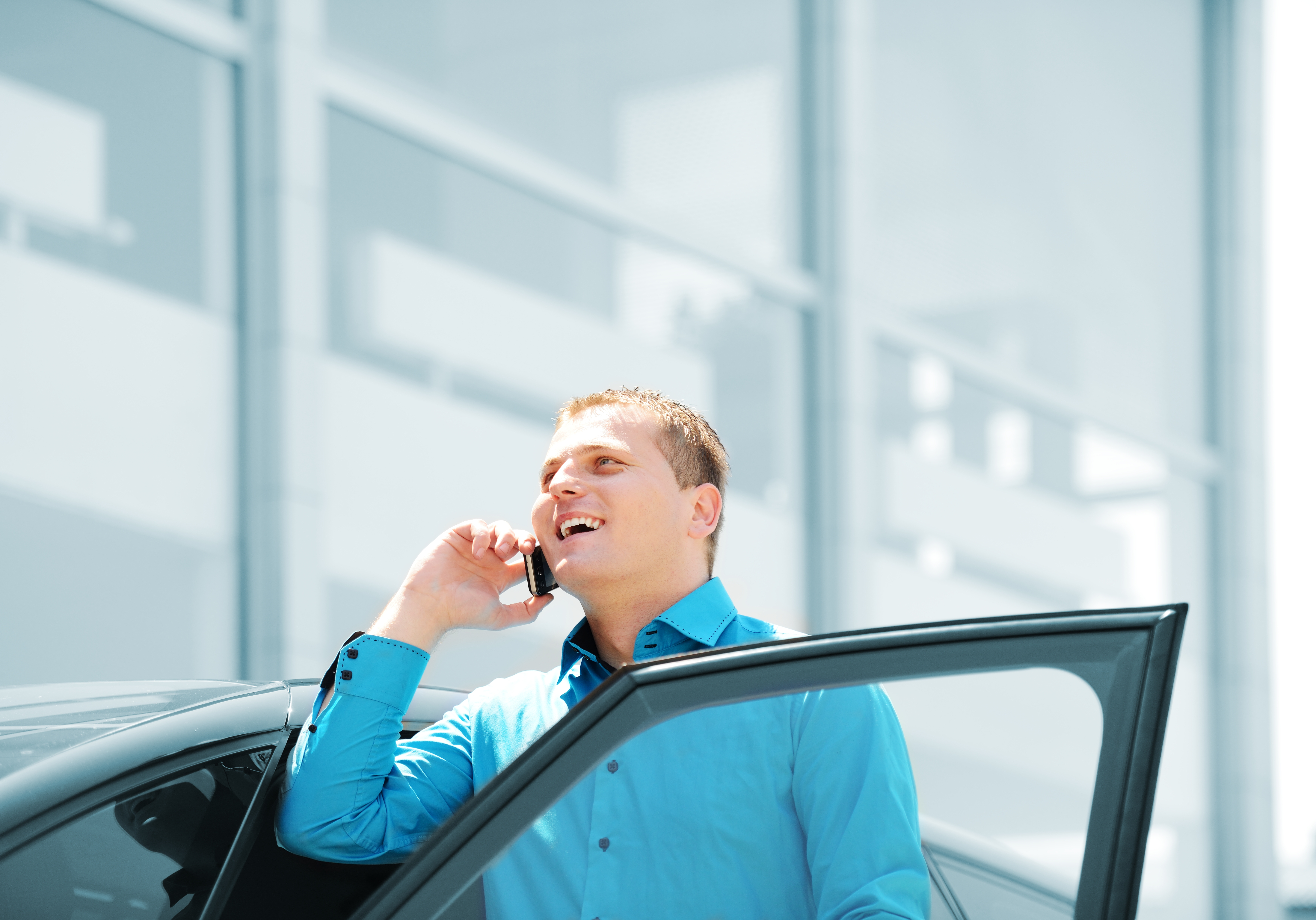 Businessman by the car car, talking on mobile phone, smiling