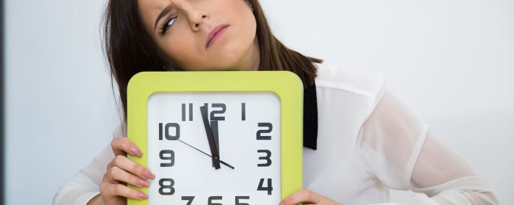 Tired businesswoman sitting at the table with clock. Waiting for break