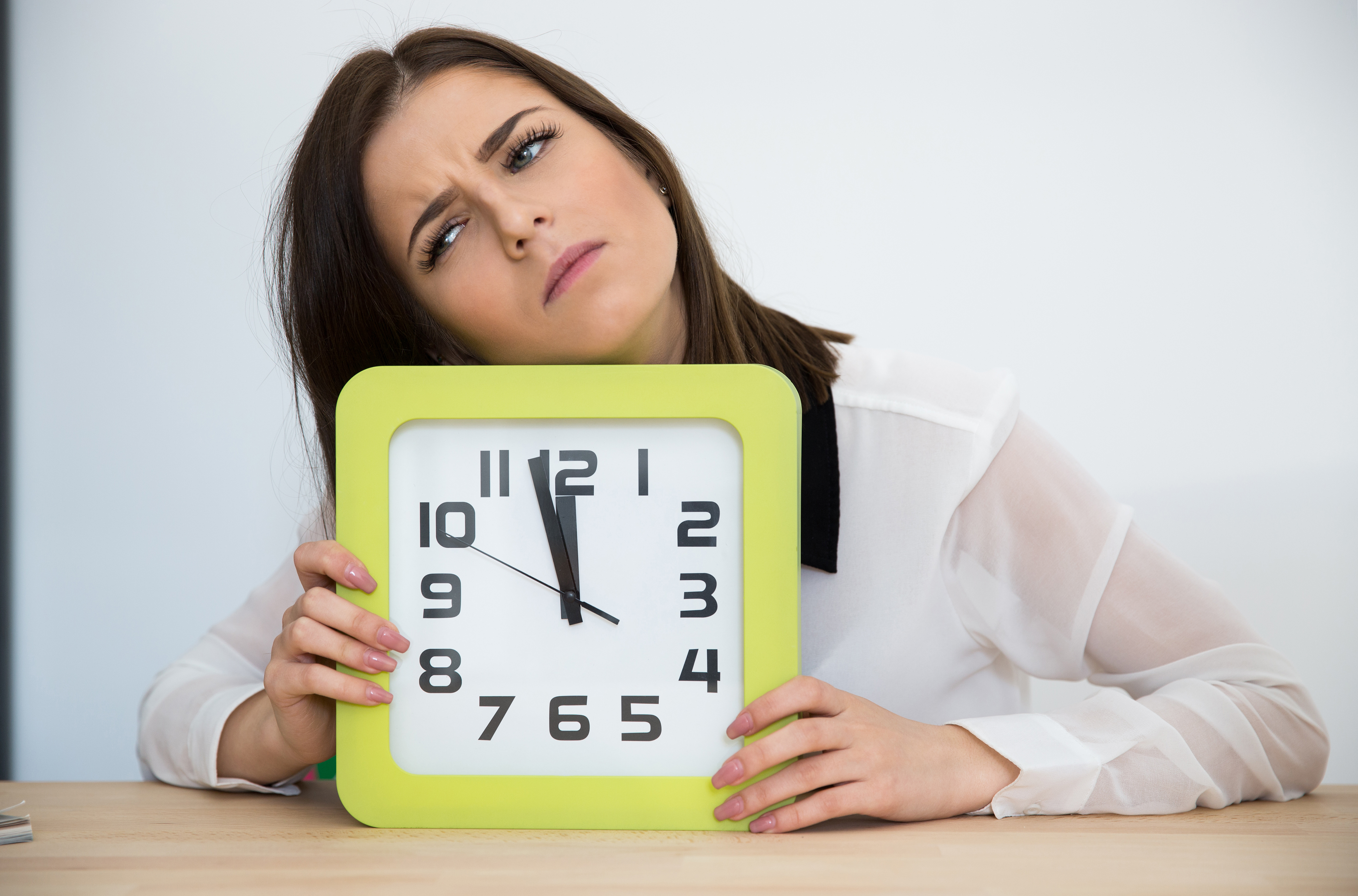 Tired businesswoman sitting at the table with clock. Waiting for break
